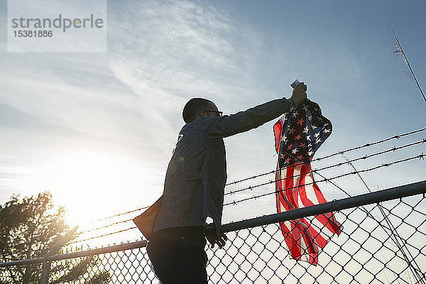 Junger Mann entfernt US-amerikanische Fahne vom Maschendrahtzaun