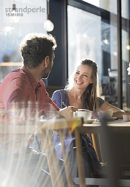 Lächelnde Frau und Mann unterhalten sich am Tisch in einem Café