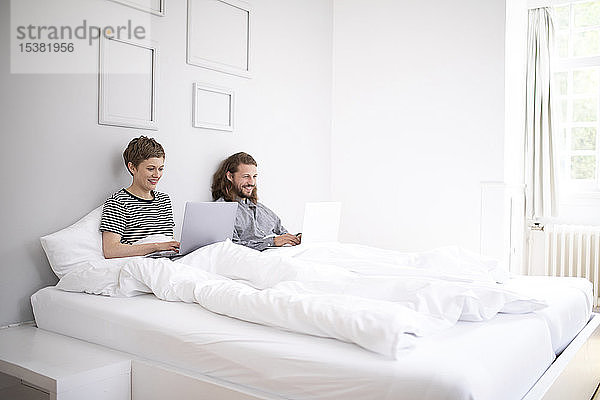 Junges Paar benutzt zu Hause Laptops im Bett