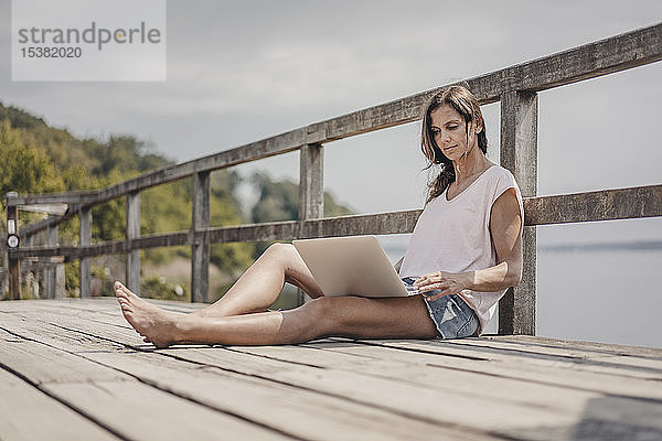 Frau sitzt auf Holzbrücke und benutzt Laptop