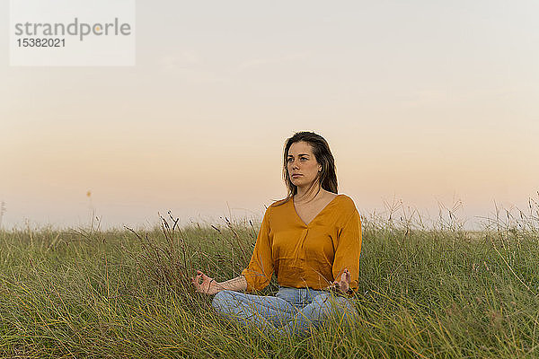 Junge Frau  die auf einer Wiese sitzt und abends meditiert