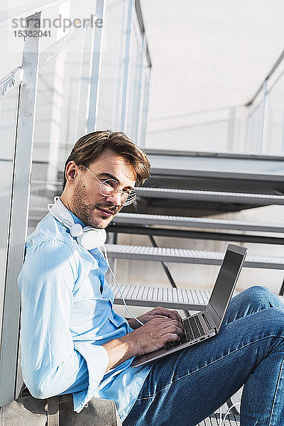 Porträt eines Gelegenheits-Geschäftsmannes  der auf einer Treppe sitzt und seinen Laptop benutzt