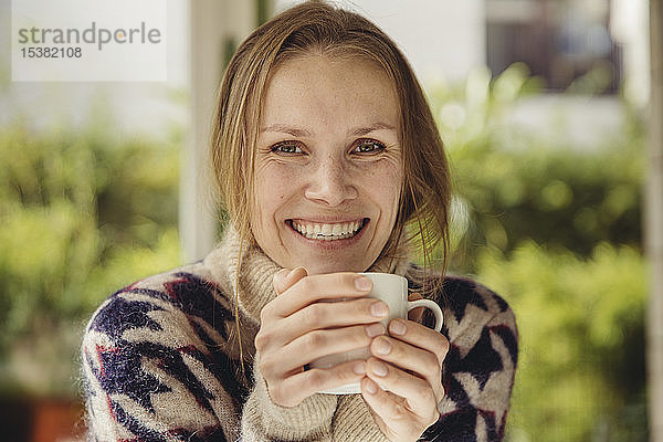 Porträt einer lächelnden jungen Frau  die einen flauschigen Pullover trägt und eine Tasse hält