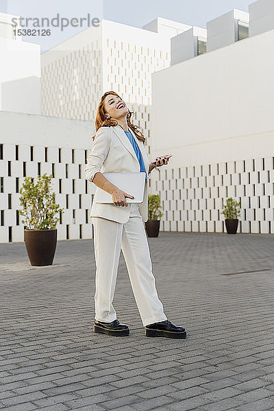 Geschäftsfrau in weißem Hosenanzug  mit Laptop  mit Smartphone