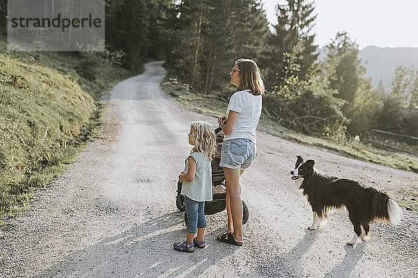 Mutter mit Tochter  Kinderwagen und Hund auf Waldweg stehend