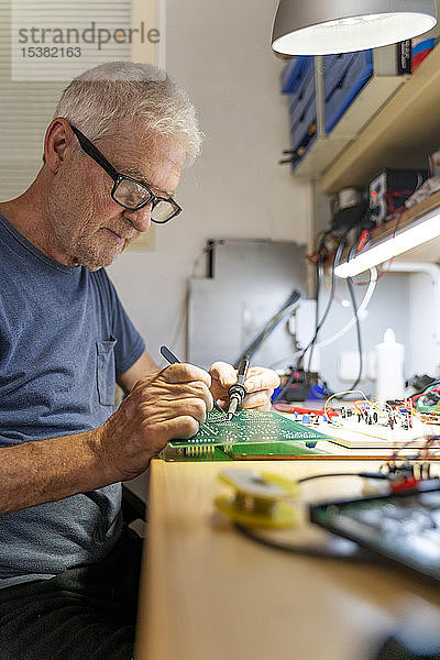 Leitender Mann  der in seiner Werkstatt an elektronischen Schaltungen arbeitet
