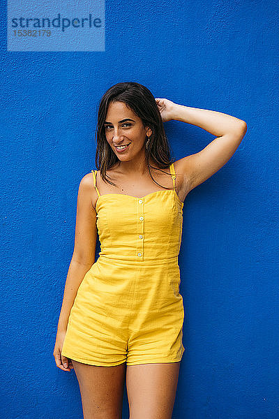 Porträt einer schönen jungen Frau in gelbem Kleid  die an einer blauen Wand posiert