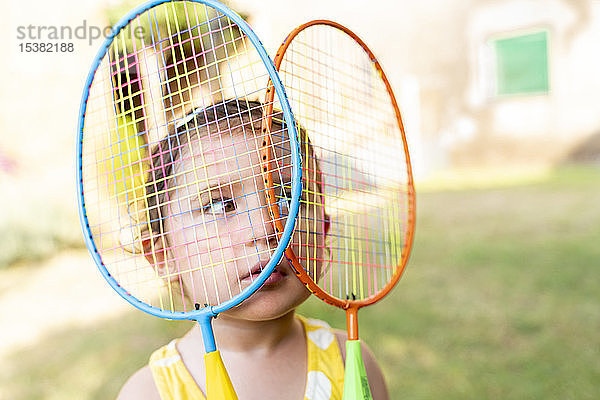 Kleines Mädchen spielt im Sommer mit bunten Badmintonschlägern im Freien