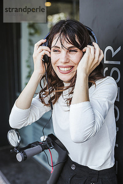 Junge Frau mit E-Scooter in der Stadt  die Musik hört