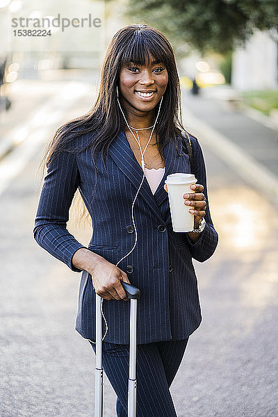 Porträt einer lächelnden Geschäftsfrau mit Koffer und Kaffee zum Draussengehen