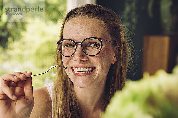 Porträt einer glücklichen jungen Frau mit Brille  die eine Gabel hält