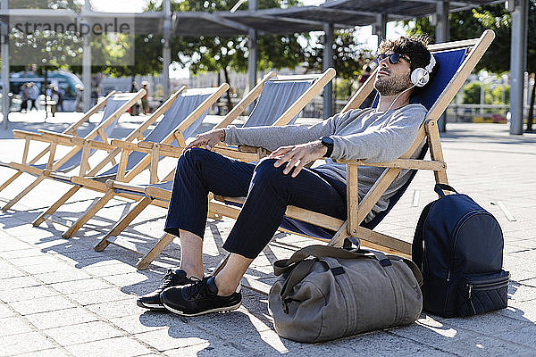Mann entspannt sich im Liegestuhl auf städtischem Platz und hört Musik