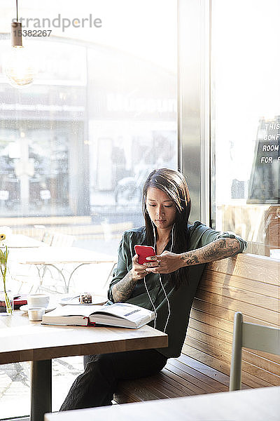 Frau mit Ohrstöpseln und Handy in einem Cafe