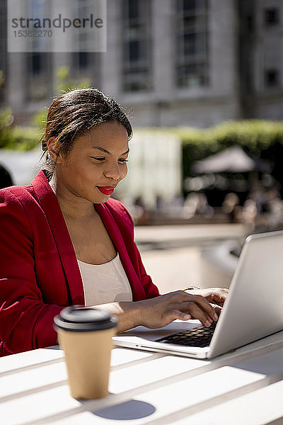 Porträt einer lächelnden Geschäftsfrau  die im Freien am Laptop arbeitet  London  UK