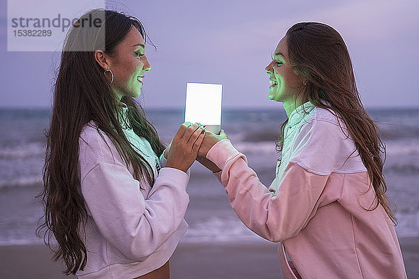 Zwei glückliche Freundinnen halten nachts am Strand lediges Licht
