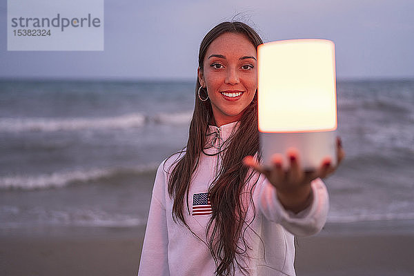 Porträt einer jungen Frau  die nachts am Strand lediges Licht hält