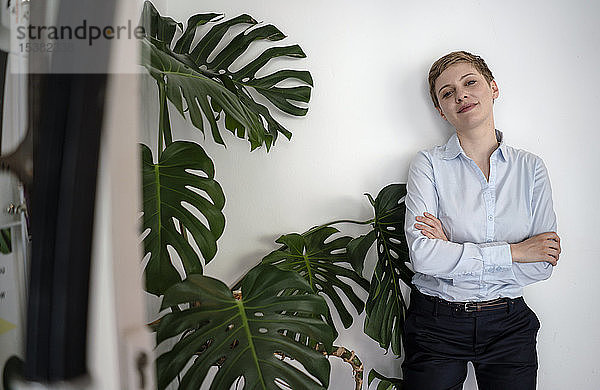 Porträt einer selbstbewussten Geschäftsfrau  die an einer Wand neben einer Pflanze steht