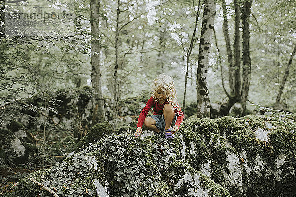 Blondes Mädchen sitzt auf einem Felsen im Wald