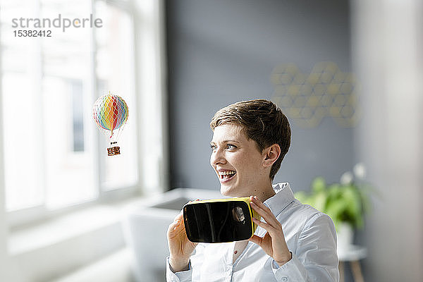 Lächelnde Frau mit VR-Brille und kleinem Heißluftballon im Büro