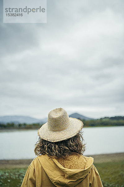 Rückansicht einer jungen Frau mit Strohhut  die auf einen See schaut
