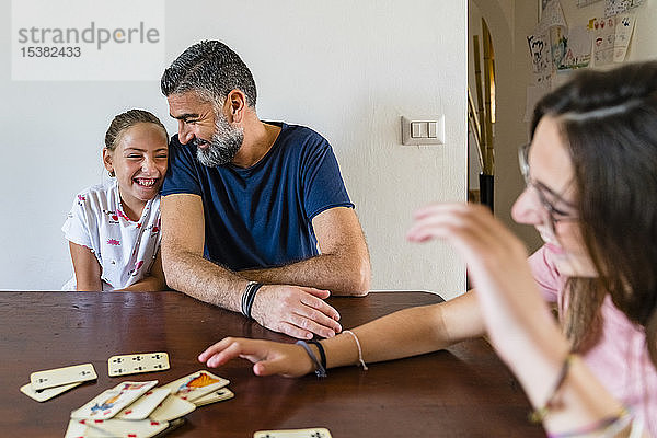 Glücklicher Vater mit zwei Töchtern  die zu Hause auf einem Holztisch Karten spielen