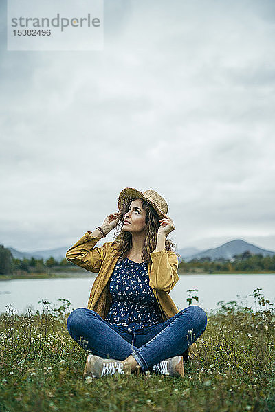 Junge Frau in gelbem Mantel sitzt auf einer Wiese und schaut auf