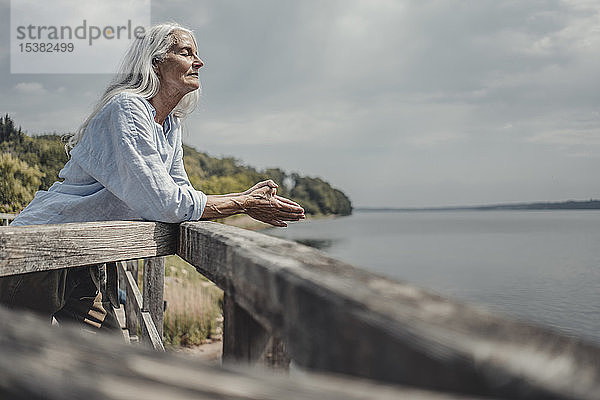 Ältere Frau steht auf der Brücke und entspannt sich mit geschlossenen Augen