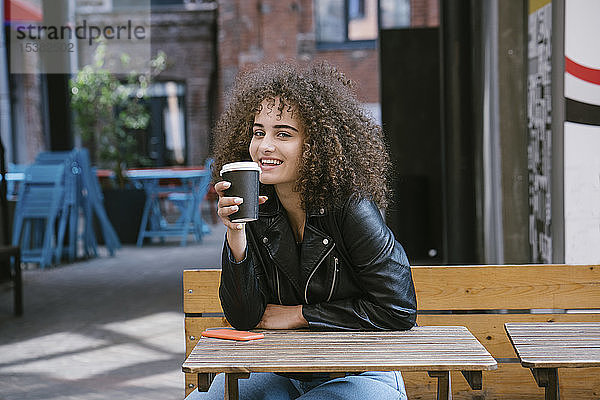 Porträt eines lächelnden Teenagers  der auf einer Bank sitzt und Kaffee zum Mitnehmen trinkt