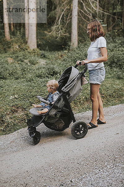 Mutter mit Tochter im Kinderwagen auf Waldweg