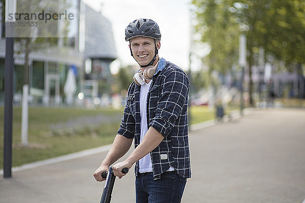 Porträt eines lächelnden jungen Mannes mit E-Scooter in der Stadt