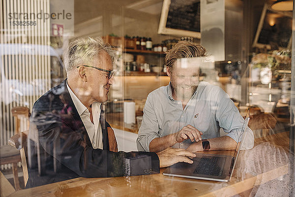 Zwei lächelnde Geschäftsleute mit Laptop treffen sich in einem Cafe