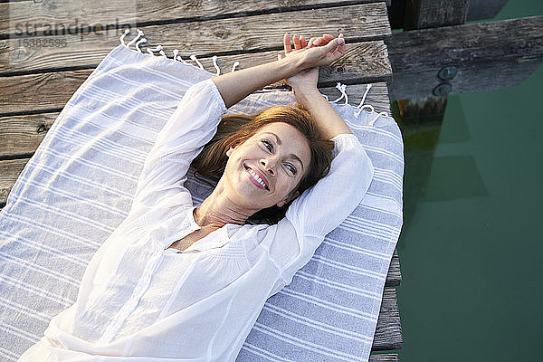 Lächelnde reife Frau  die auf einem Handtuch auf einem Steg an einem See liegt