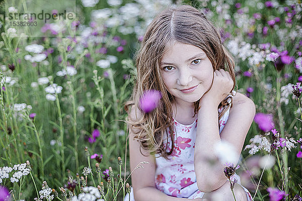 Porträt eines lächelnden Mädchens auf einer Blumenwiese sitzend