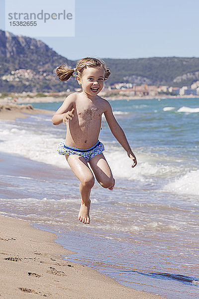 Porträt eines glücklichen kleinen Mädchens  das am Strand in die Luft springt  Girona  Spanien