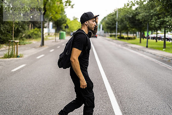 Junger Mann mit Rucksack überquert eine Straße in der Stadt
