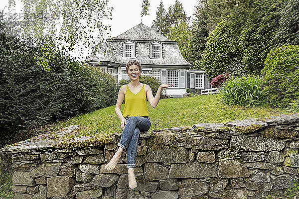 Glückliche Frau sitzt auf einer Mauer im Garten