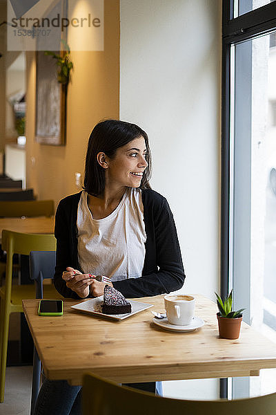 Lächelnde junge Frau in einem Cafe  die aus dem Fenster schaut