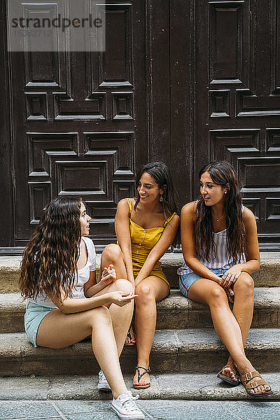 Drei Freundinnen sitzen auf einer Treppe und unterhalten sich