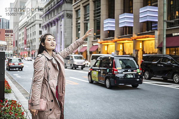 Junge Frau  die an einer Straße in Ginza  Tokio  Japan  ein Taxi ruft