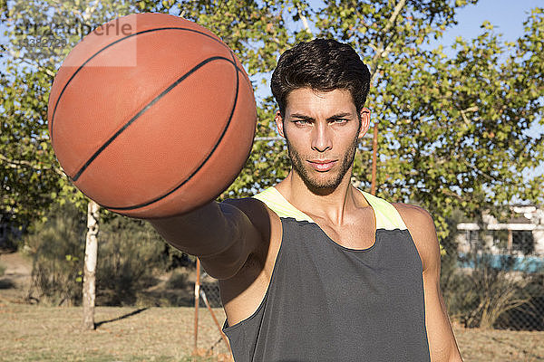Junger ernsthafter Mann in Sportkleidung streckt Hand mit Basketball aus und schaut in die Kamera