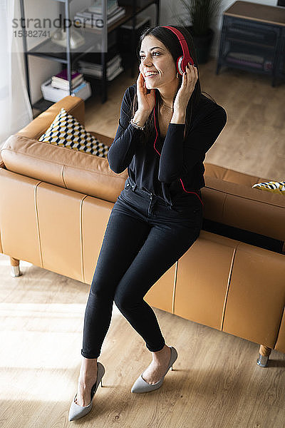 Porträt einer glücklichen jungen Frau  die zu Hause mit Kopfhörern Musik hört