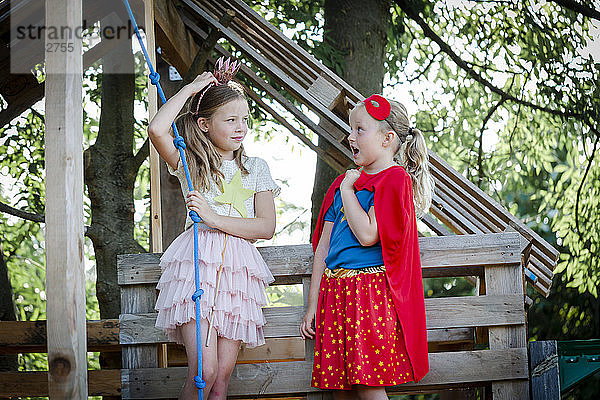 Als Prinzessin und Superwoman verkleidete Mädchen spielen in einem Baumhaus