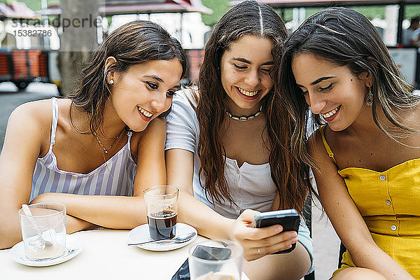 Drei glückliche Freundinnen  die sich in einem Café in der Stadt ein Handy teilen