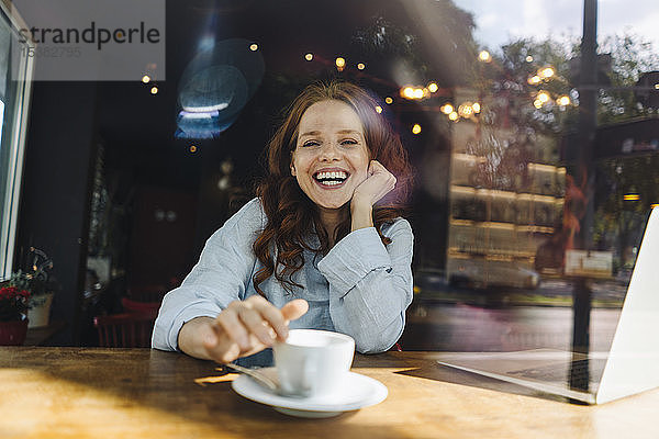 Porträt einer glücklichen rothaarigen Frau mit Laptop in einem Cafe