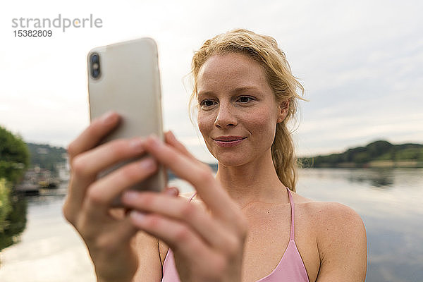Junge Frau telefoniert mit ihrem Handy an einem See