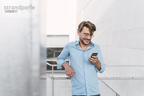 Lächelnder Gelegenheits-Geschäftsmann benutzt Mobiltelefon im Freien