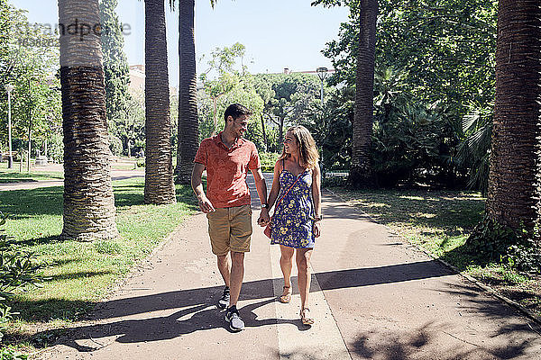 Lächelndes junges Paar geht Hand in Hand durch einen Park