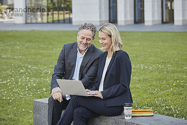 Geschäftsfrau und Geschäftsmann sitzen mit Laptop an einer Wand in der Stadt