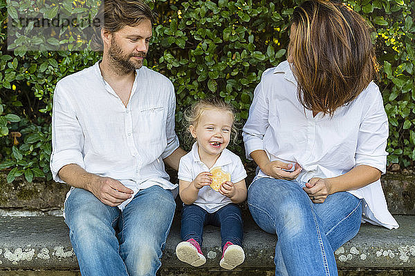 Eltern mit glücklicher kleiner Tochter auf einer Bank sitzend