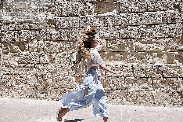 Glückliche junge Frau läuft an einer Mauer entlang